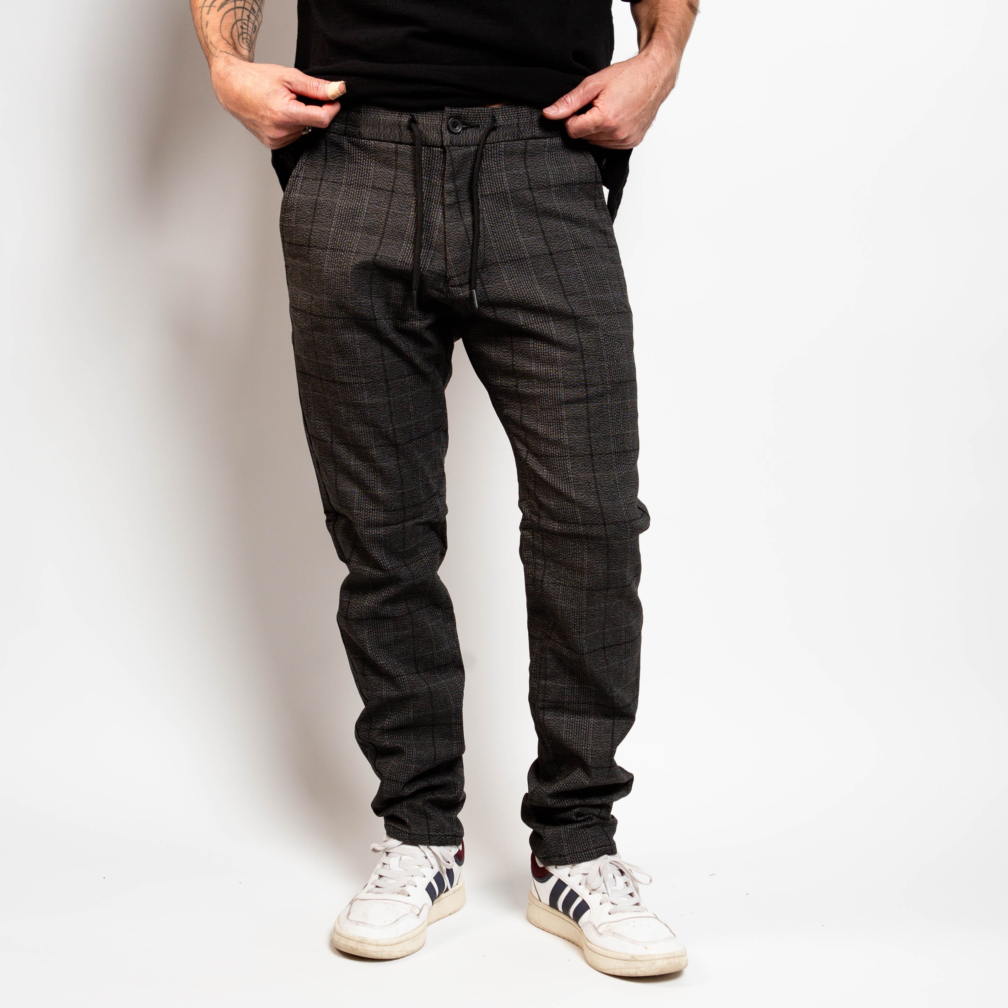 Person wearing plaid pants and white sneakers against a plain background By Projek Raw