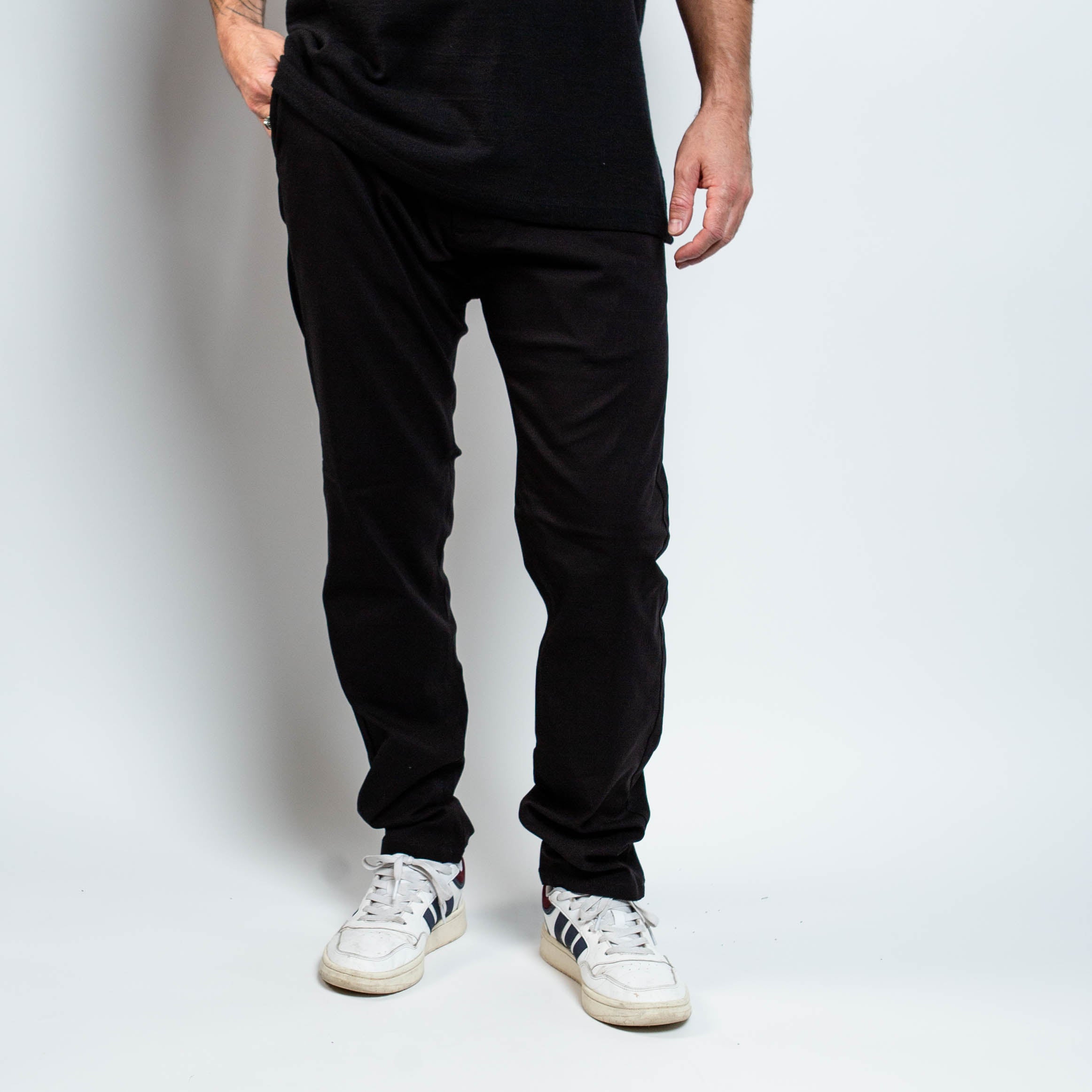 Person wearing black pants and white sneakers on a plain background By Projek Raw