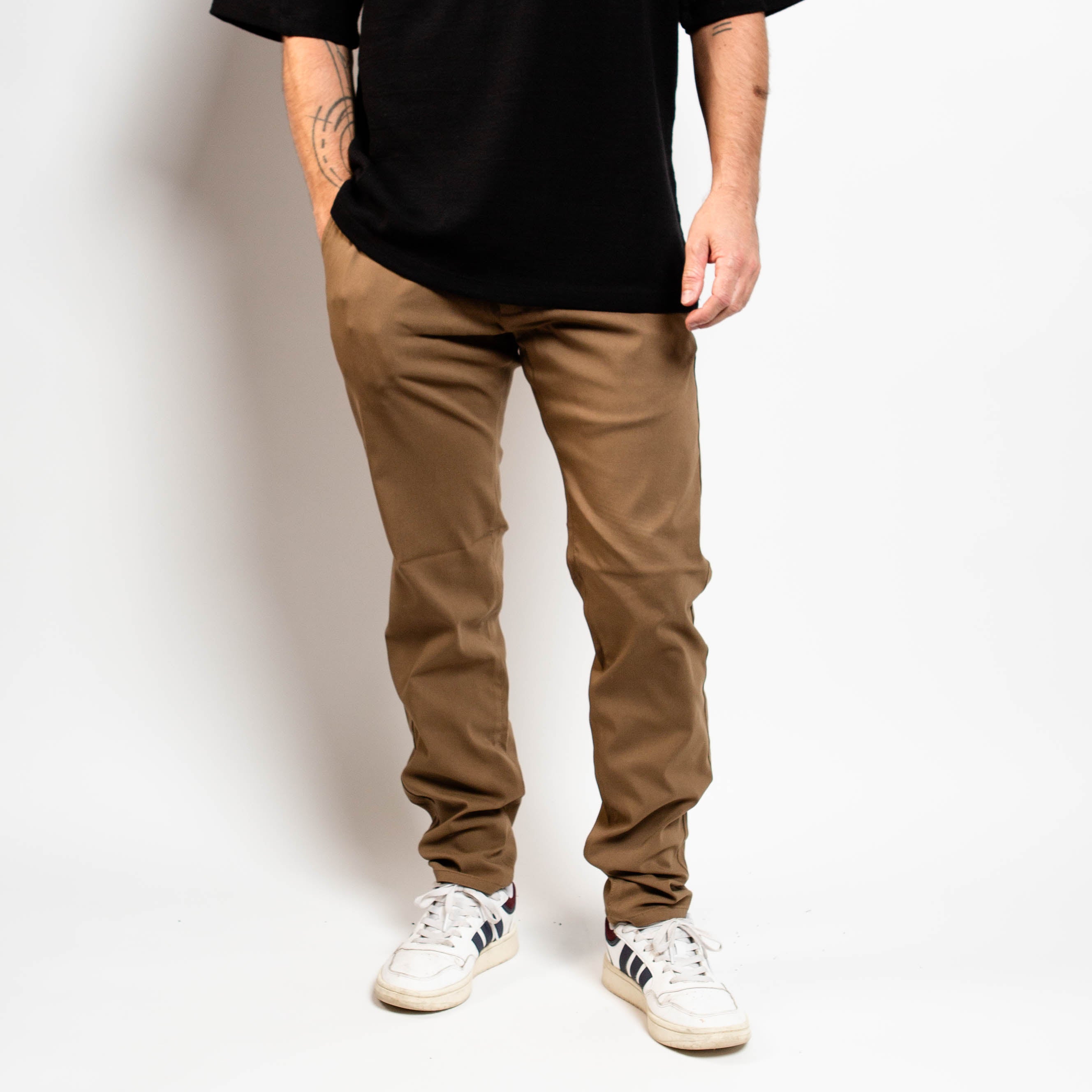 Person wearing brown pants and white sneakers on a plain background By ProjeK Raw