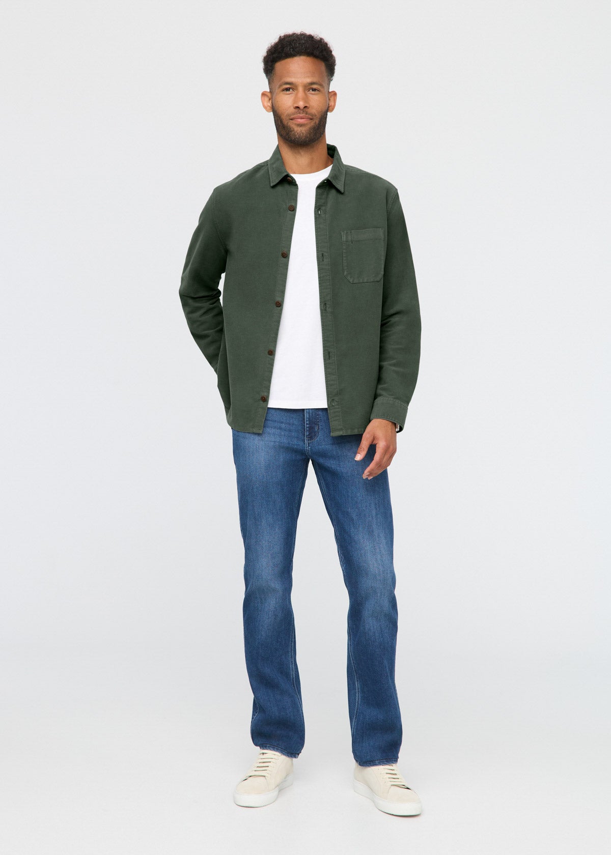 Man wearing a green jacket, white shirt, blue jeans, and white sneakers on a white background By Duer Jeans