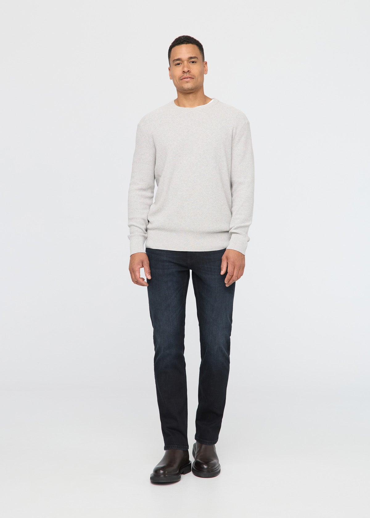 Man wearing a light gray sweater and dark jeans on a white background By Duer Jeans