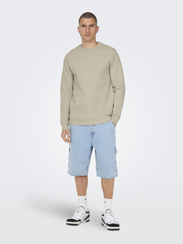 Man wearing a beige sweatshirt and light blue shorts on a white background By Only & Sons