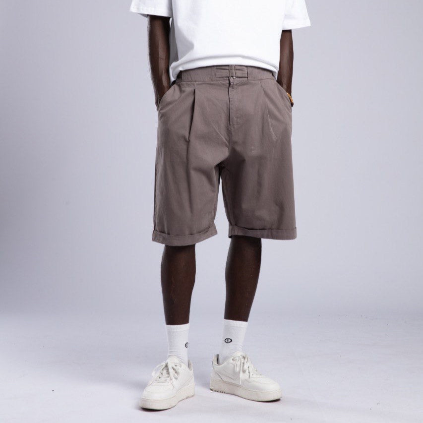 Man wearing a white t-shirt, brown shorts, and white sneakers on a gray background