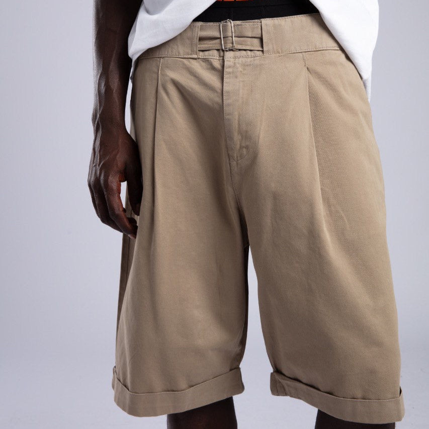 Person wearing beige shorts and a white shirt with a visible brand logo on a light gray background