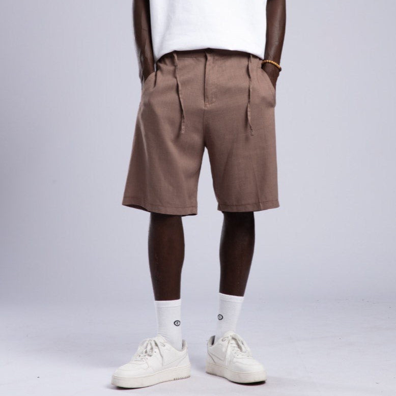 Man wearing a white t-shirt, brown shorts, and white sneakers on a gray background