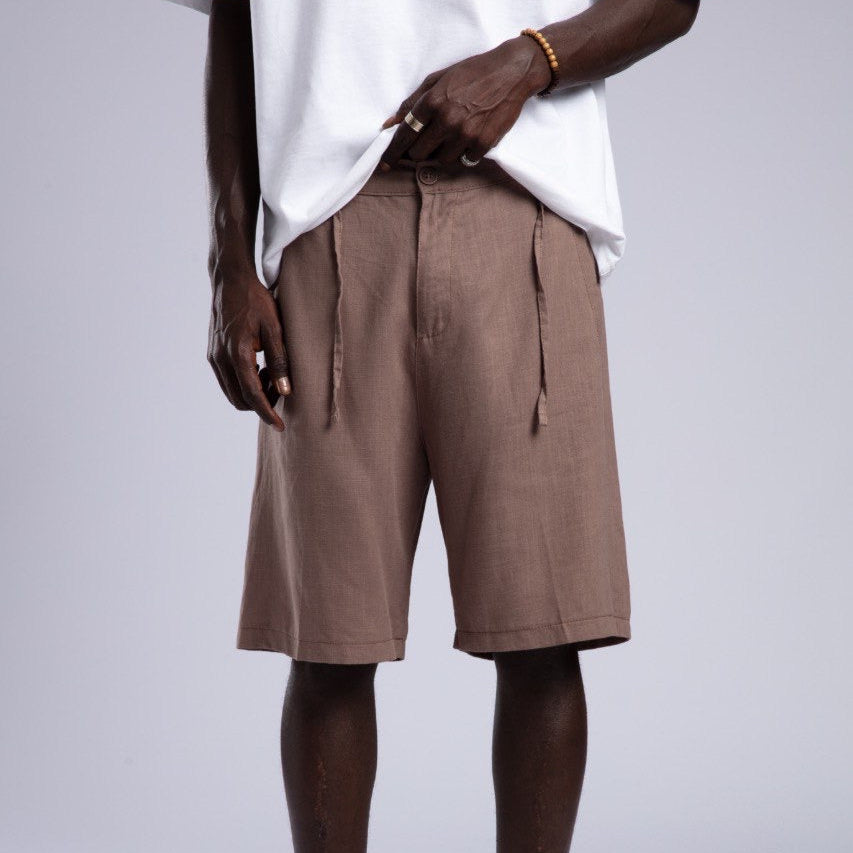 Person wearing brown shorts, white shirt, and white sneakers on a plain background