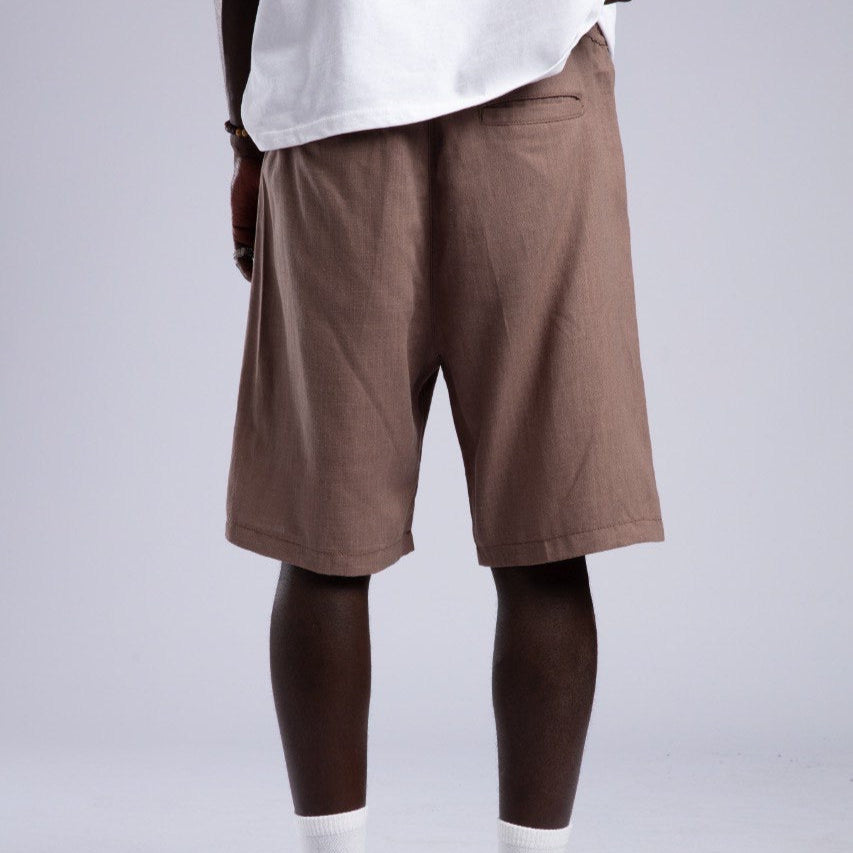 Person wearing brown shorts, white shirt, and white shoes on a plain background