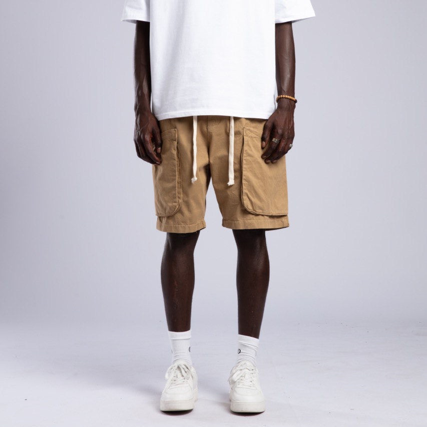 Man wearing a white t-shirt and beige cargo shorts on a gray background