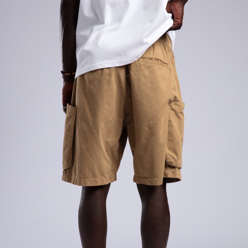 Person wearing beige cargo shorts and white sneakers on a plain background