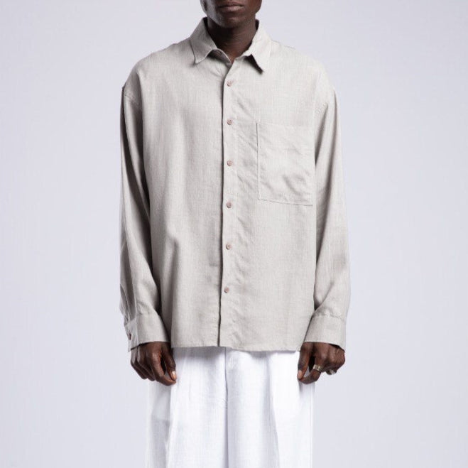 Man wearing a beige button-up shirt and white pants on a white background