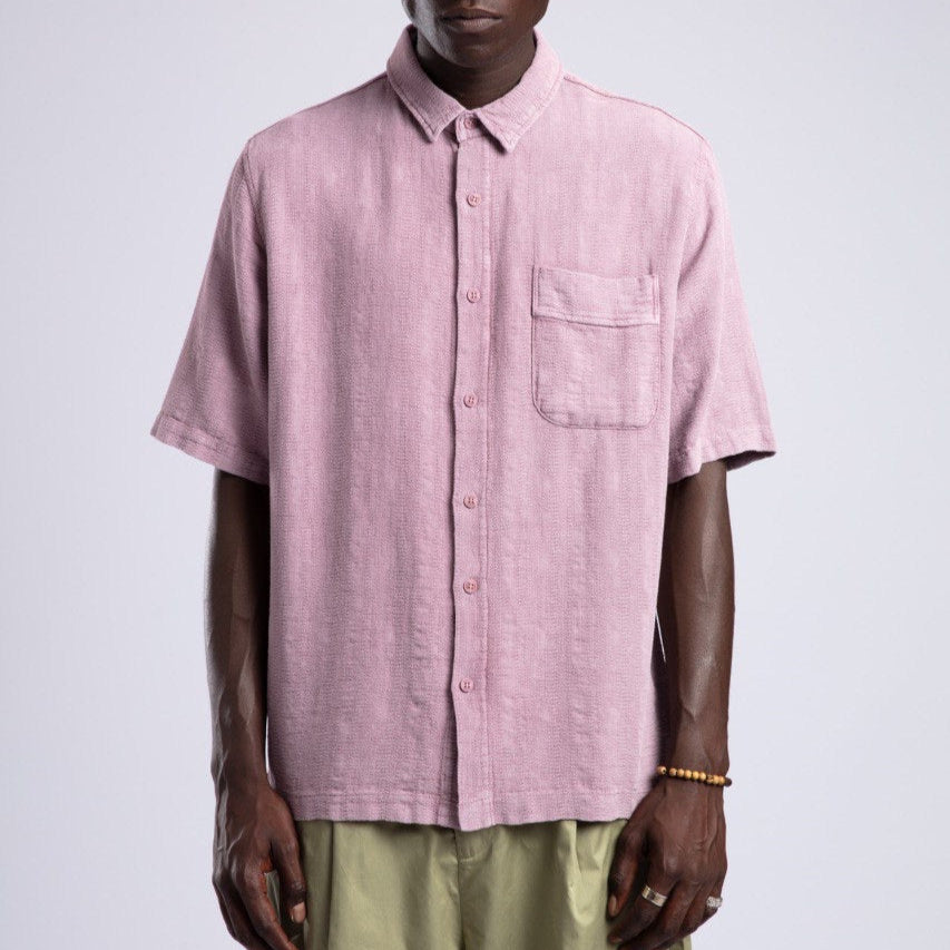 Man wearing a pink short-sleeve shirt and sunglasses against a white background