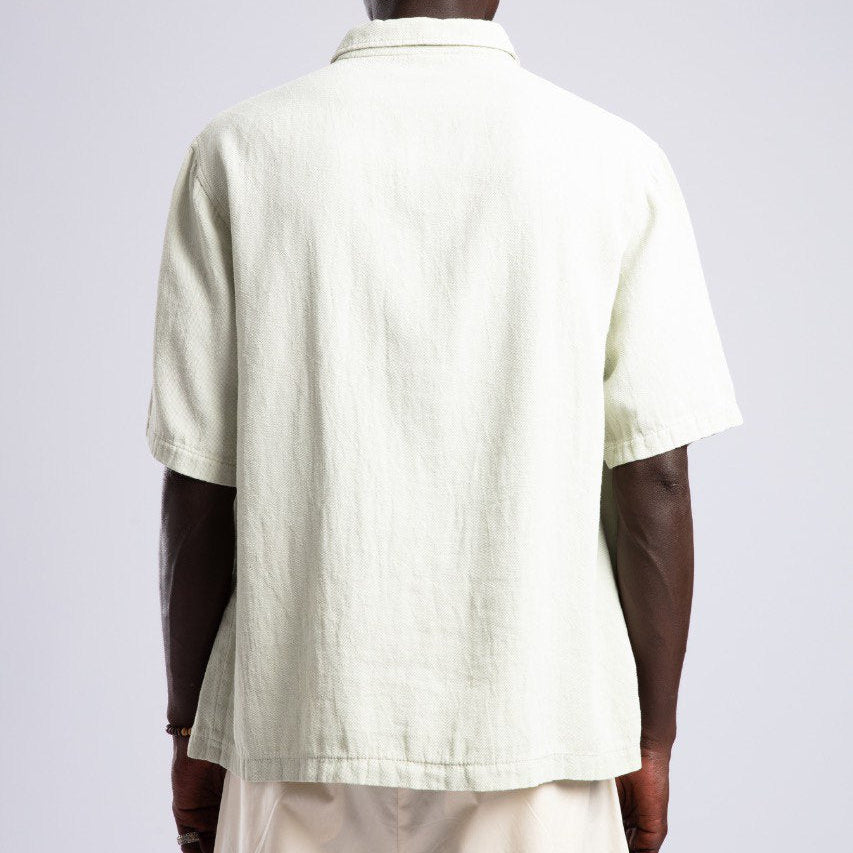 Man wearing a light green shirt and beige pants against a white background