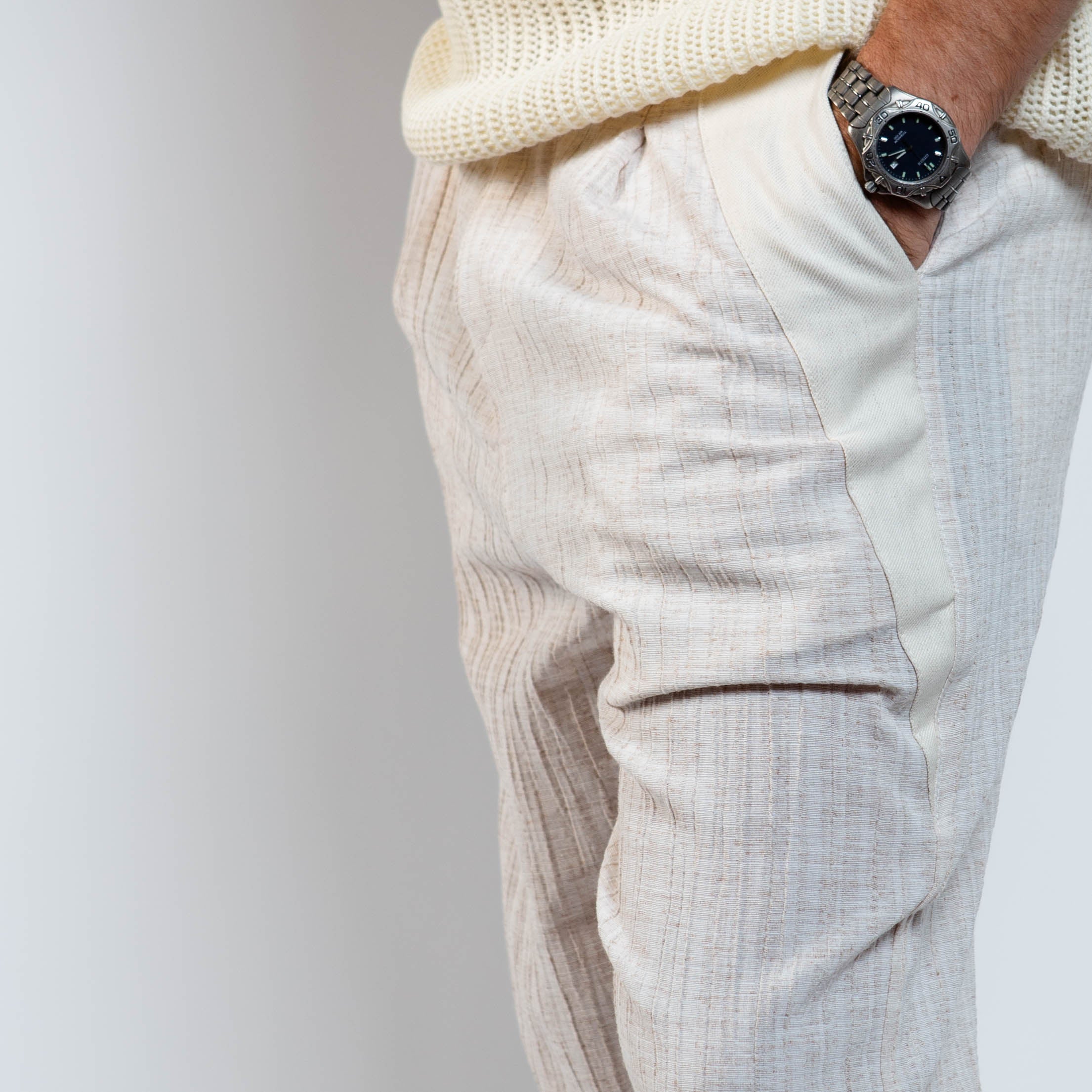 Person wearing light-colored pants and a watch on a plain background