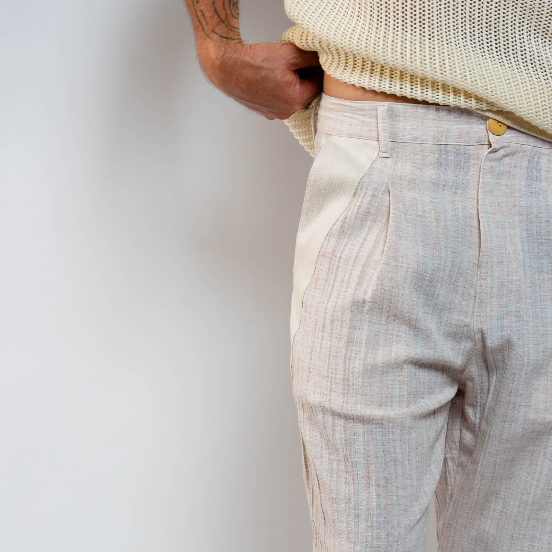 Person wearing light-colored pants and a beige sweater against a plain background