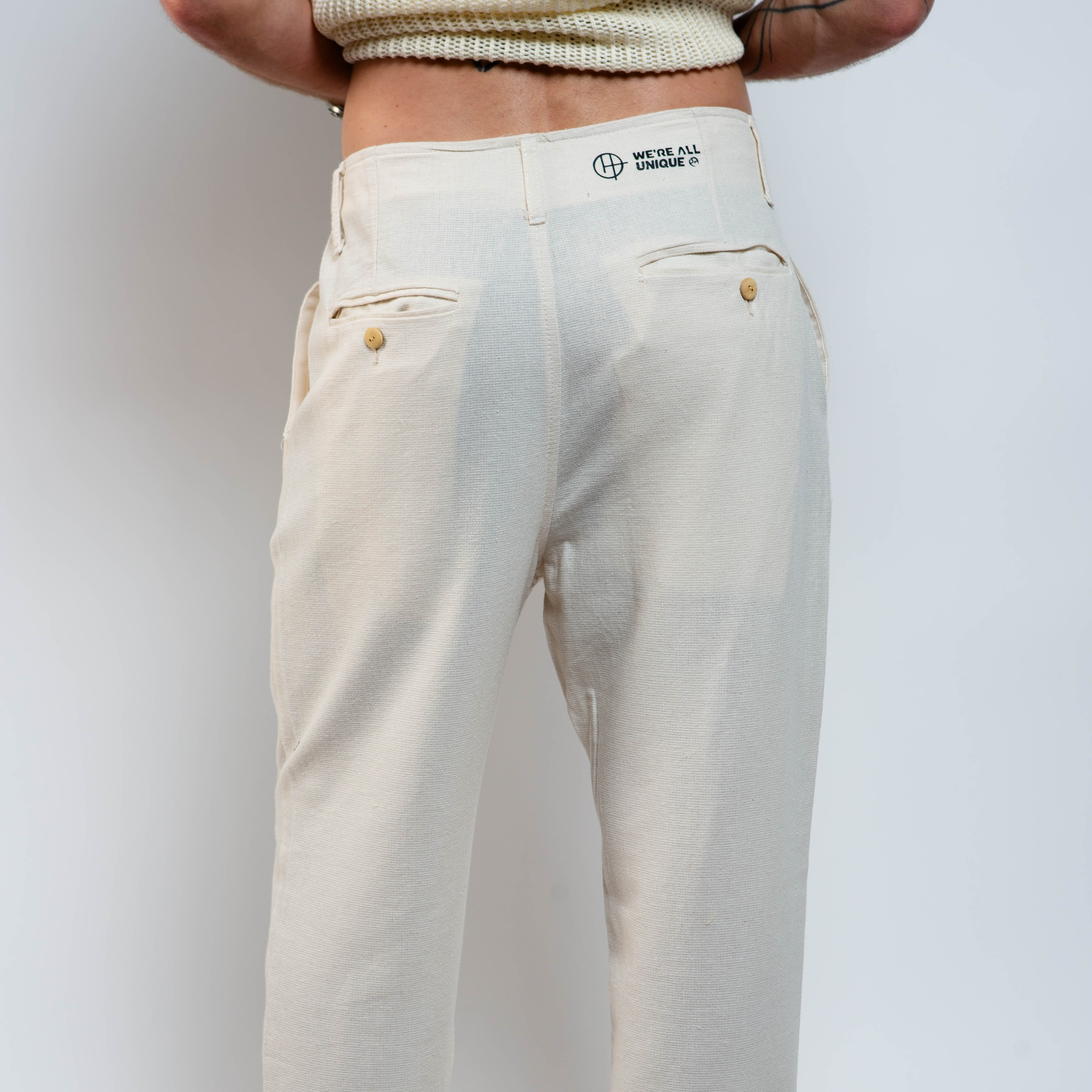 Person wearing beige pants with a visible brand logo on a plain background
