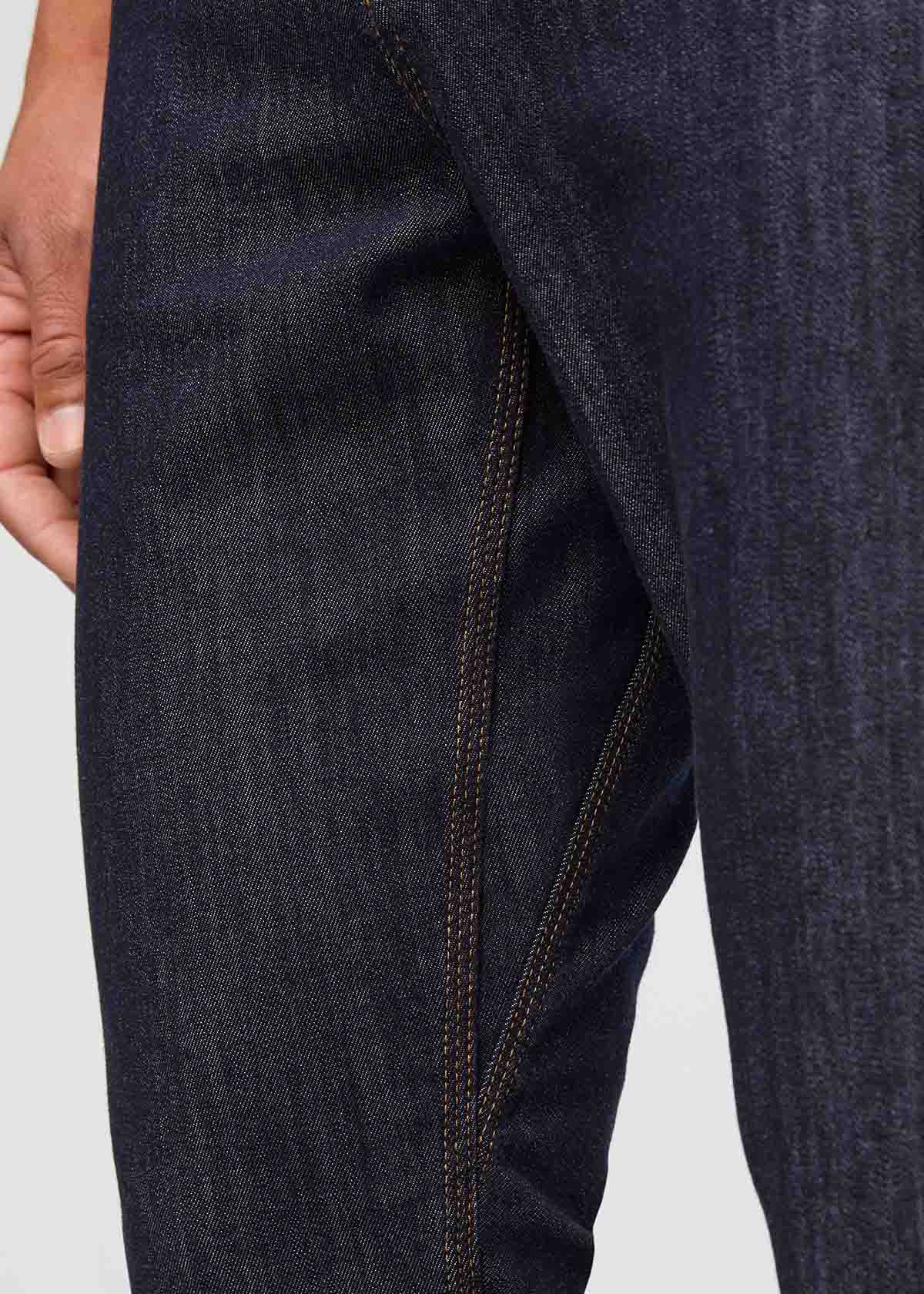 Close-up of dark blue jeans with visible stitching on a light gray background By Duer Jeans