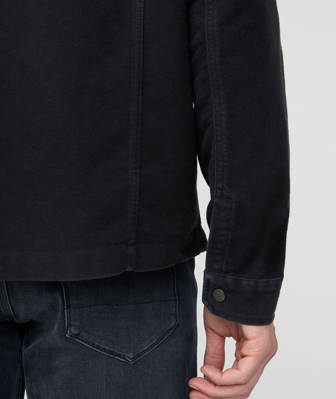 Person wearing a black jacket and dark jeans on a light gray background By Duer Jeans