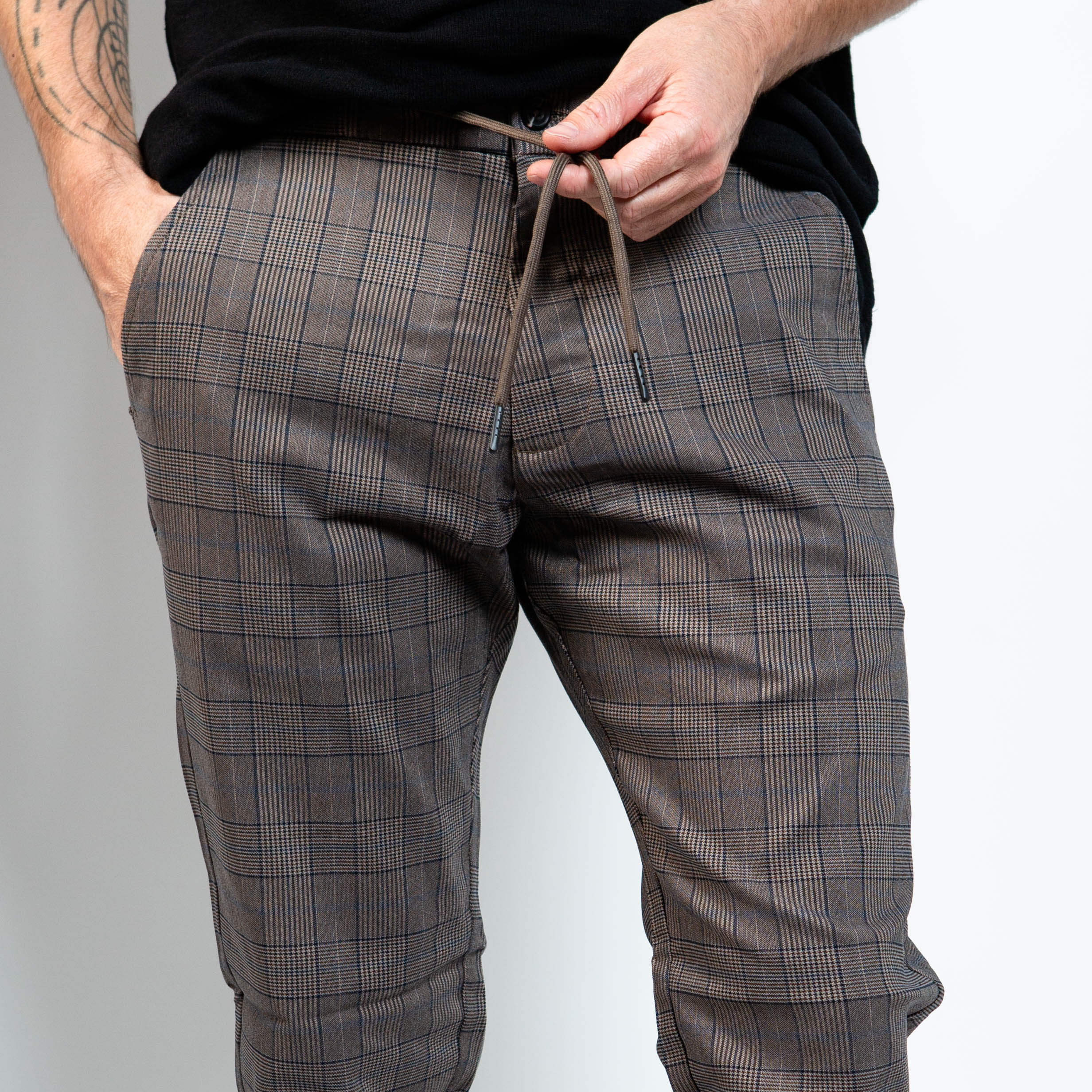 Person wearing gray plaid pants with a plain background By Projek Raw