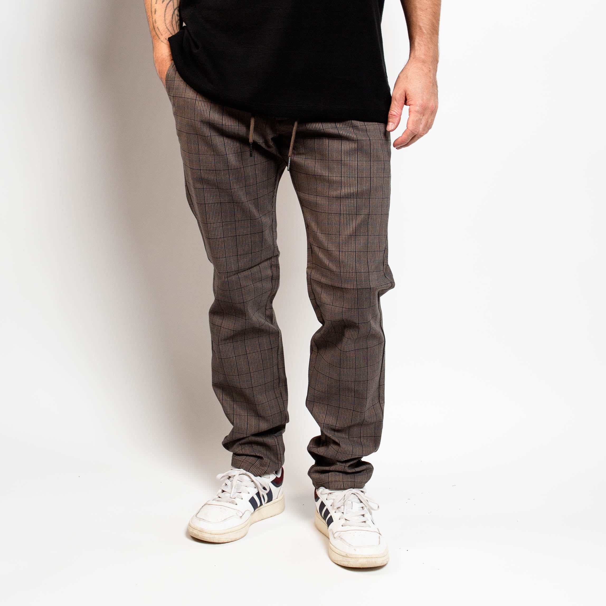 Person wearing gray checkered pants and white sneakers on a plain background By Projek Raw