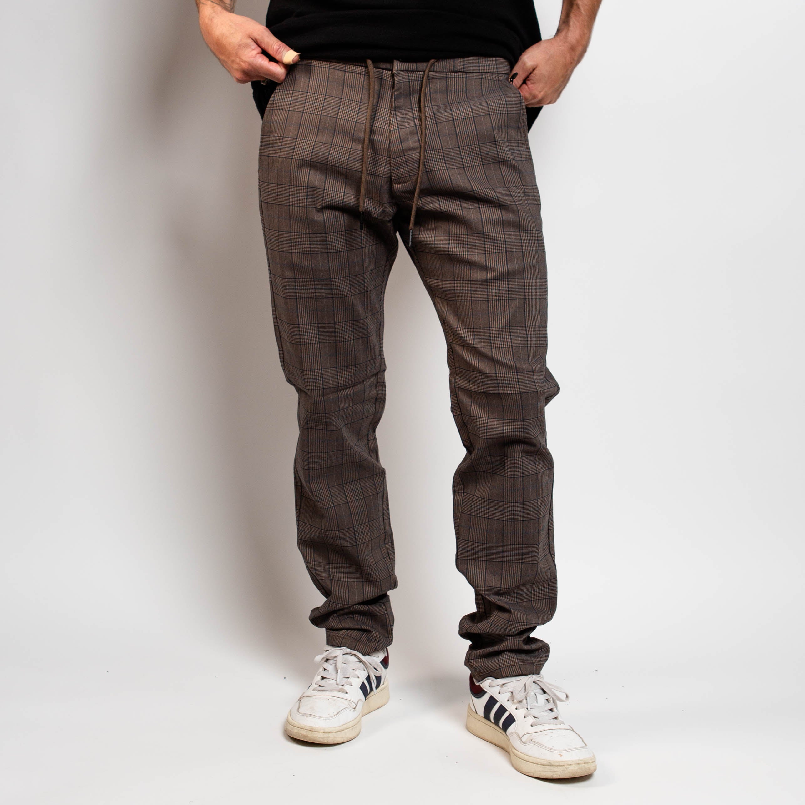 Person wearing brown plaid pants and white sneakers on a plain background By Projek Raw