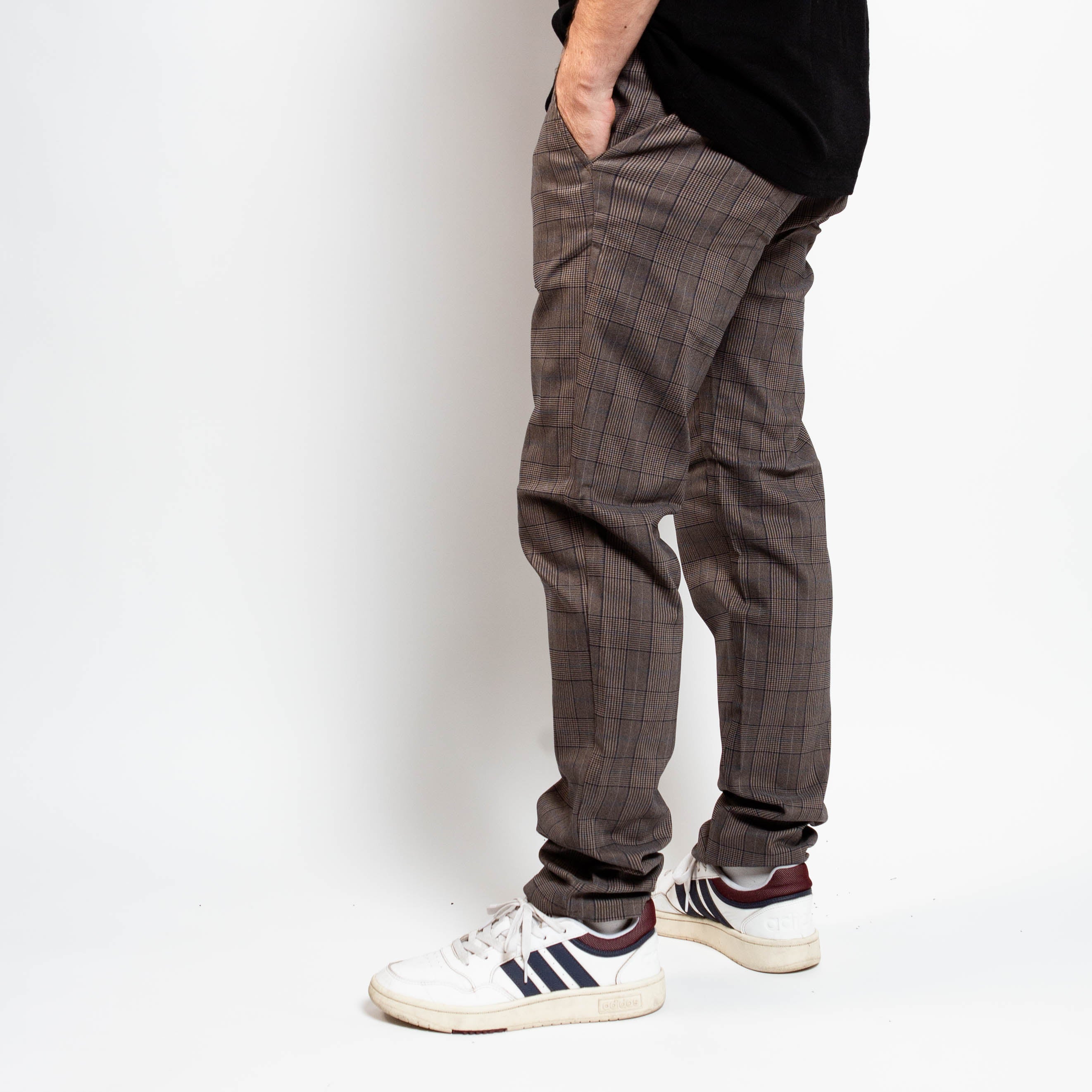 Person wearing plaid pants and white sneakers on a plain background By Projek Raw