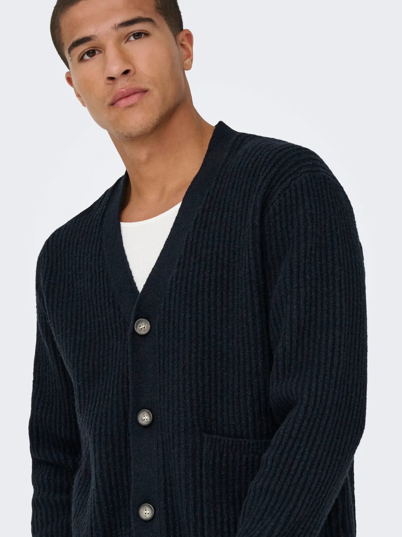 Man wearing a dark blue cardigan over a white shirt on a light gray background by only and sons