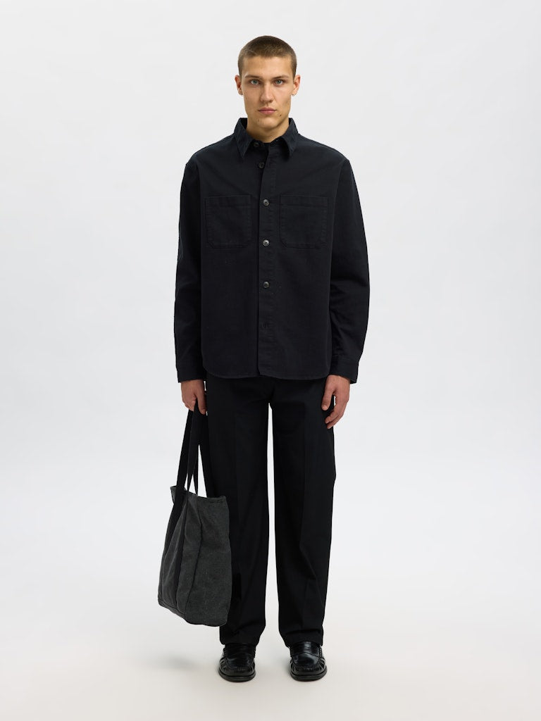 Male model wearing a black Twill overshirt by SELECTED Homme, featuring button-up front, two chest pockets, and a relaxed minimalist fit.