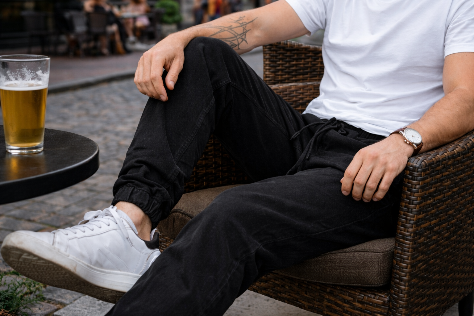 Close up of black jogger pants worn by a male model sitting on a summer patio in Gastown, showing elastic cuffs, drawstring waist, and relaxed fit styling