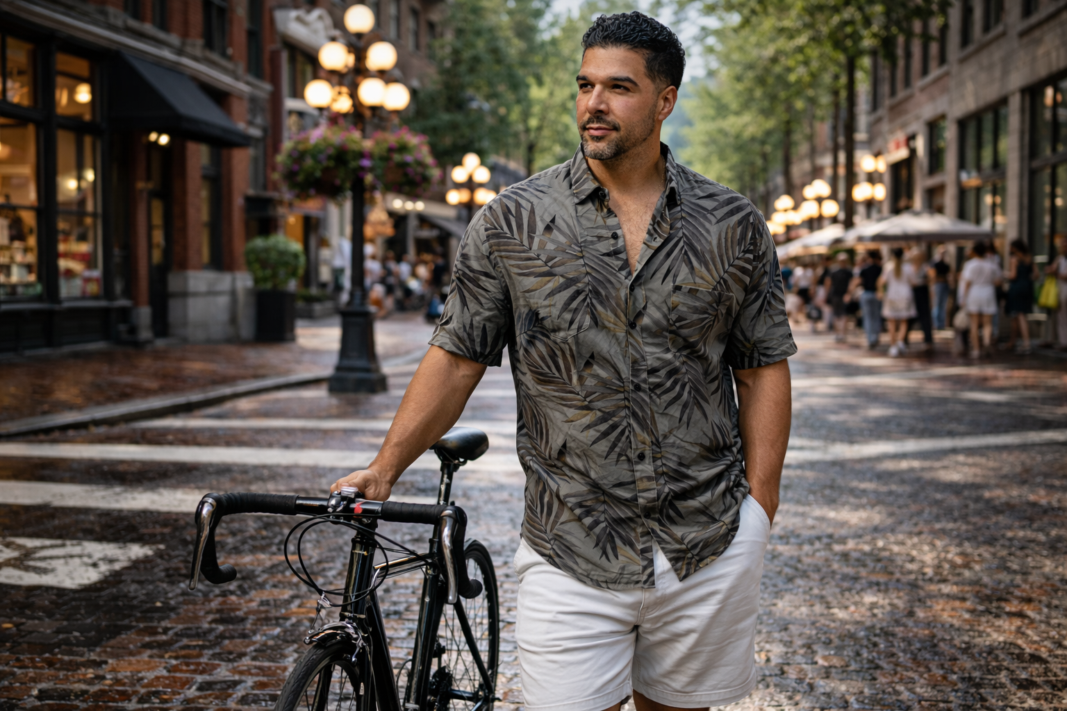 male model wearing a patterned short sleeve shirt with white shorts walking his bike down gastown street in summer vancouver