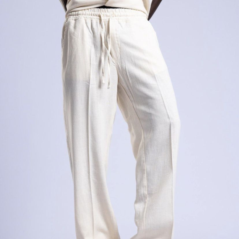 Person wearing a beige outfit with white pants on a light gray background