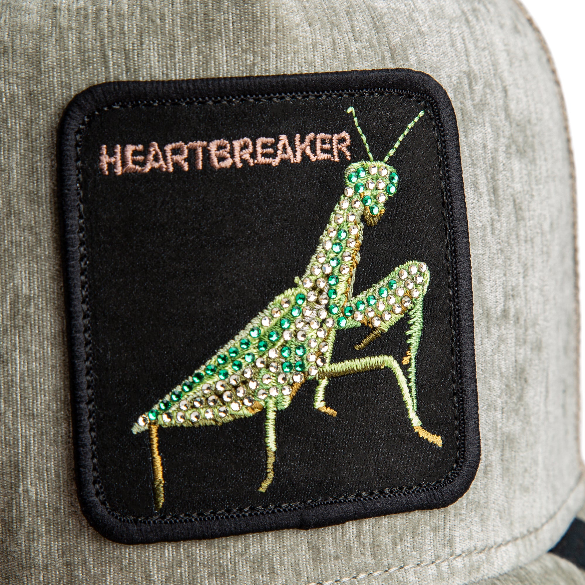 Patch of a praying mantis with 'HEARTBREAKER' text on a black background, attached to a gray fabric surface.