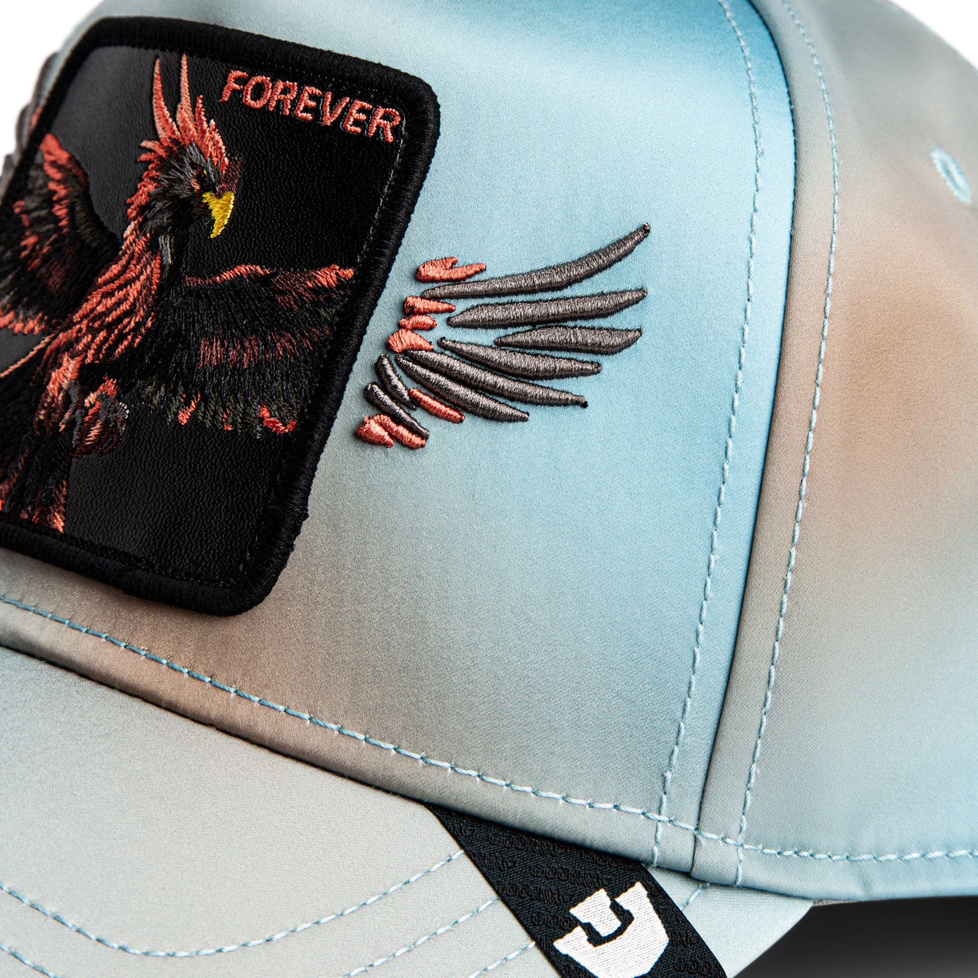 Close-up of a cap with an embroidered eagle design and 'FOREVER' text on a light blue background.