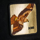 Embroidered patch of a hawk with 'BOMB' text on a beige background, attached to a black surface.