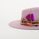 Pink hat with decorative band and feather on a white background