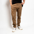 Person wearing brown pants and white sneakers on a plain background By Projek Raw