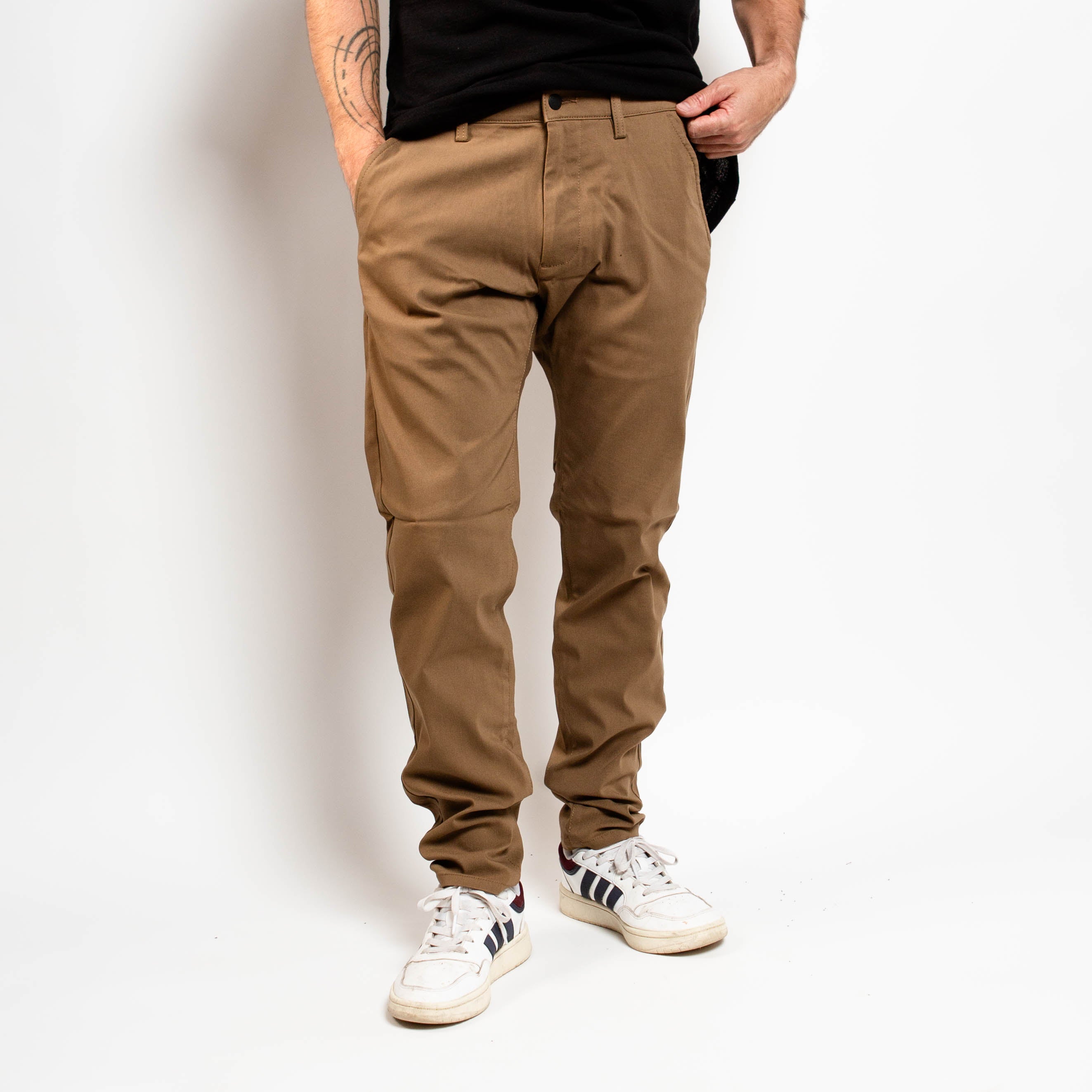 Person wearing brown pants and white sneakers on a plain background By Projek Raw