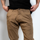 Person wearing brown pants and a black shirt against a plain background By Projek Raw