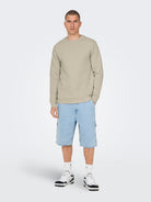 Man wearing a beige sweatshirt and light blue shorts on a white background By Only & Sons