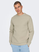Man wearing a beige sweatshirt on a light gray background By Only & Sons