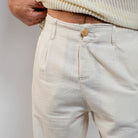 Beige pants with a button worn by a person on a plain background
