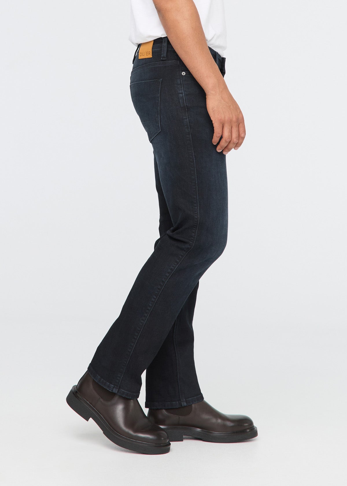 Person wearing dark blue jeans and brown shoes on a white background By Duer Jeans