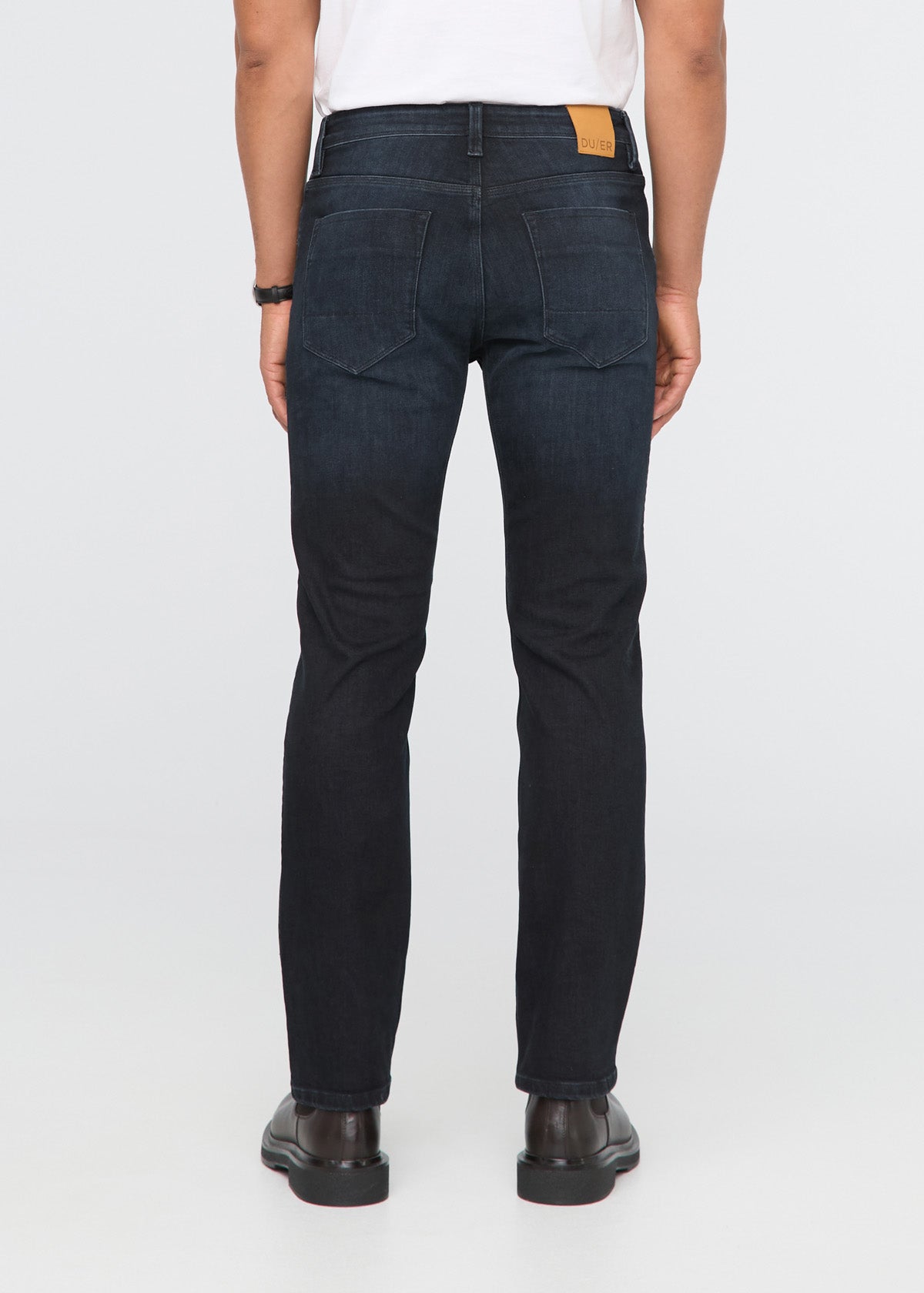 Person wearing dark blue jeans on a white background By Duer Jeans