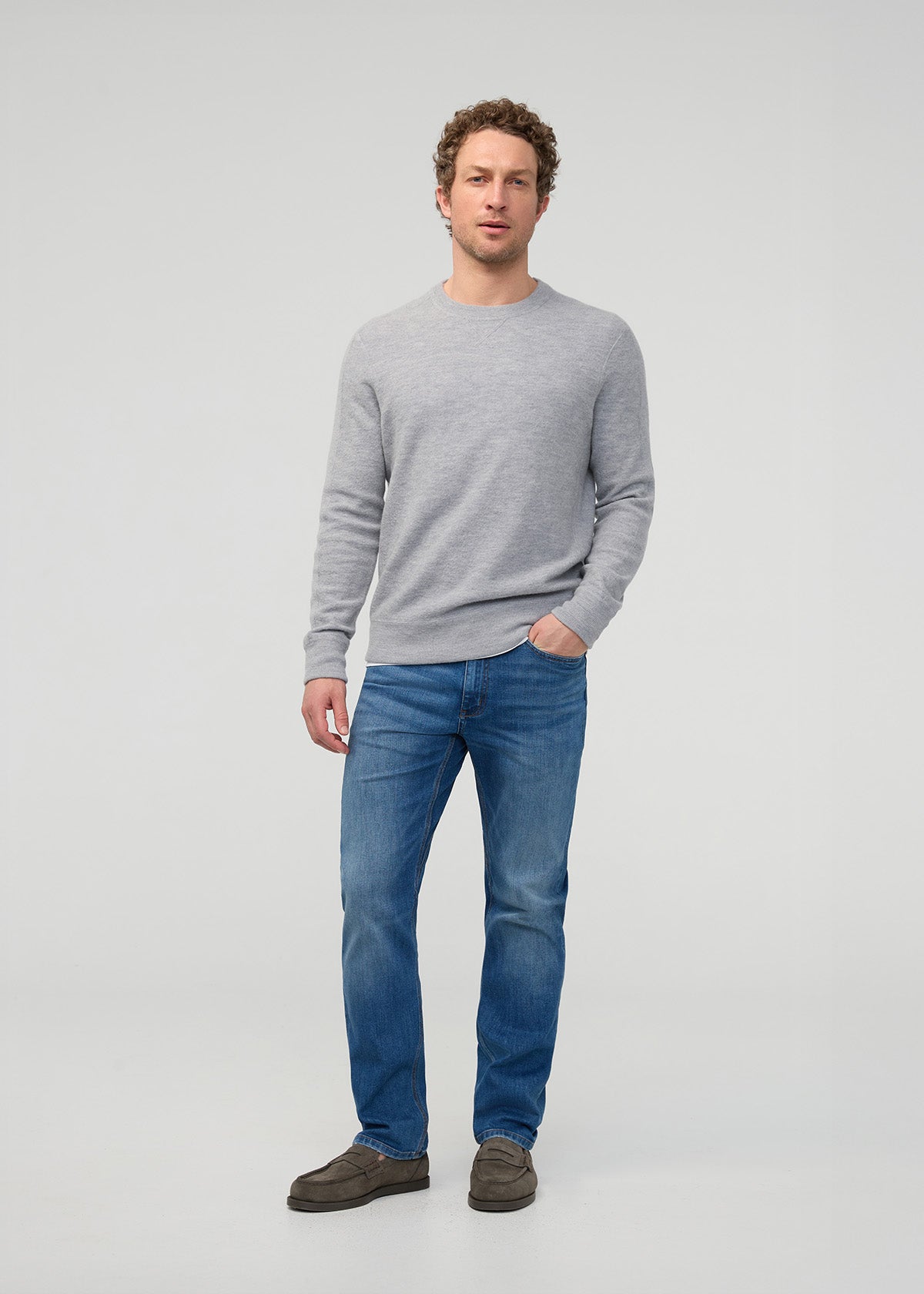 Man wearing a gray sweater and blue jeans on a light gray background By Duer Jeans