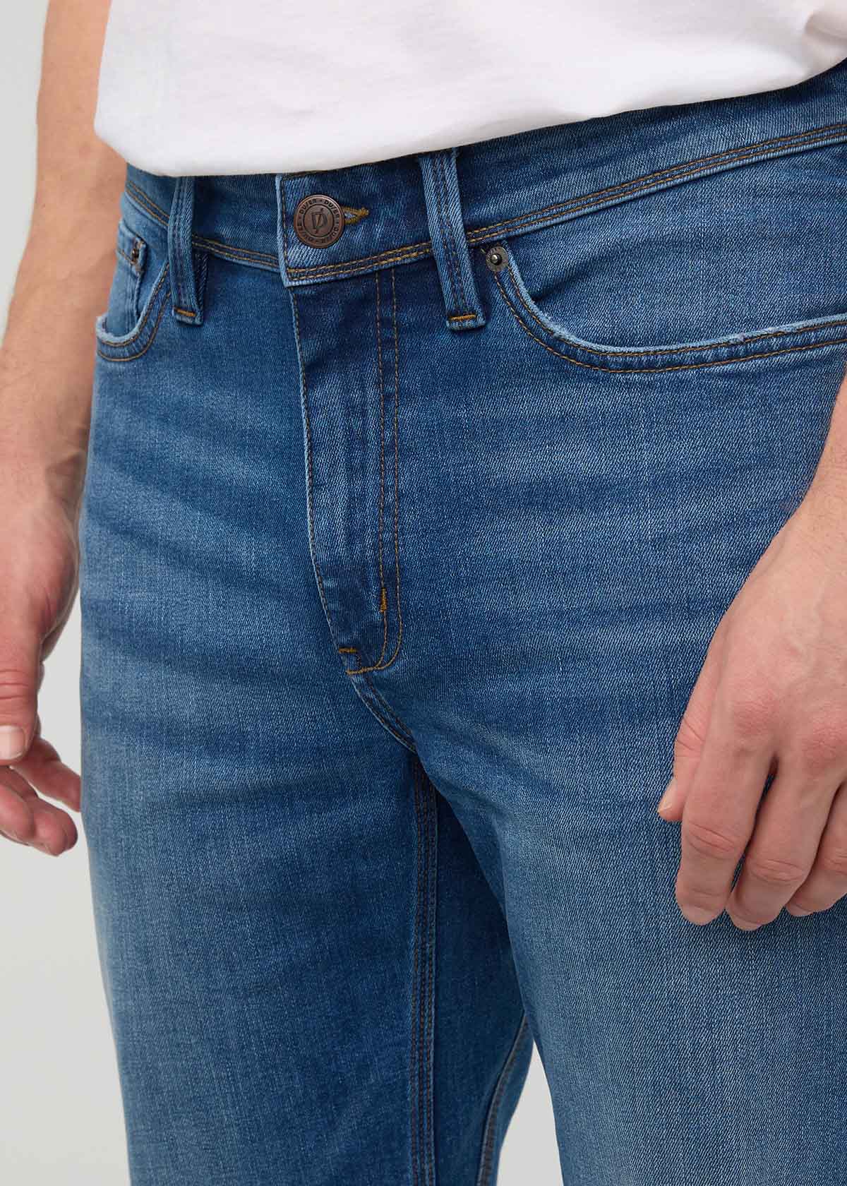 Close-up of blue jeans with a white shirt underneath on a plain background By Duer Jeans