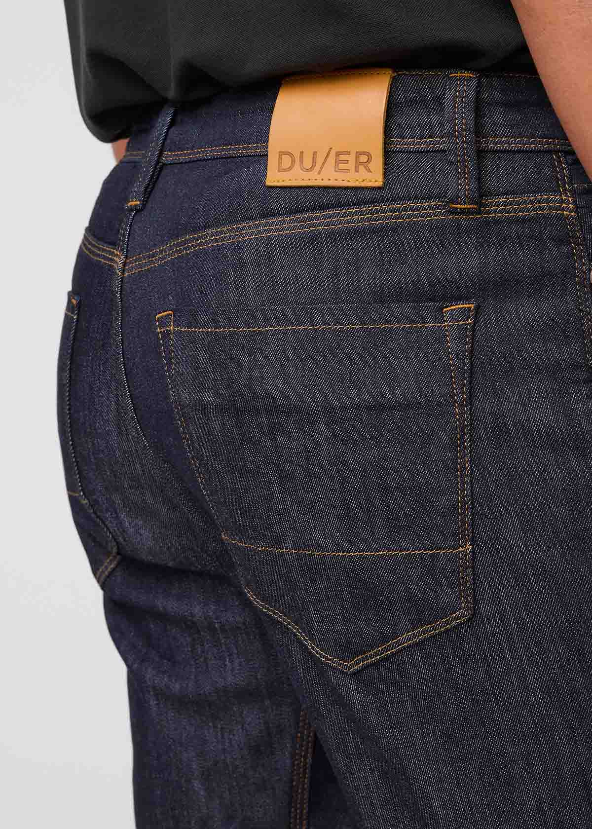 Close-up of dark blue jeans with a visible brand label on a light gray background By Duer Jeans