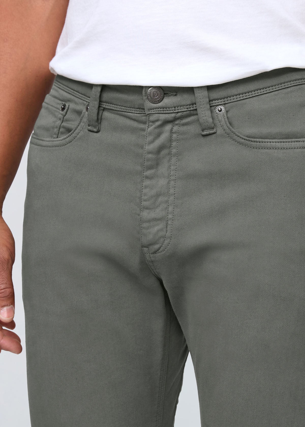 Close-up of gray pants with a white shirt underneath on a light gray background By Duer Jeans