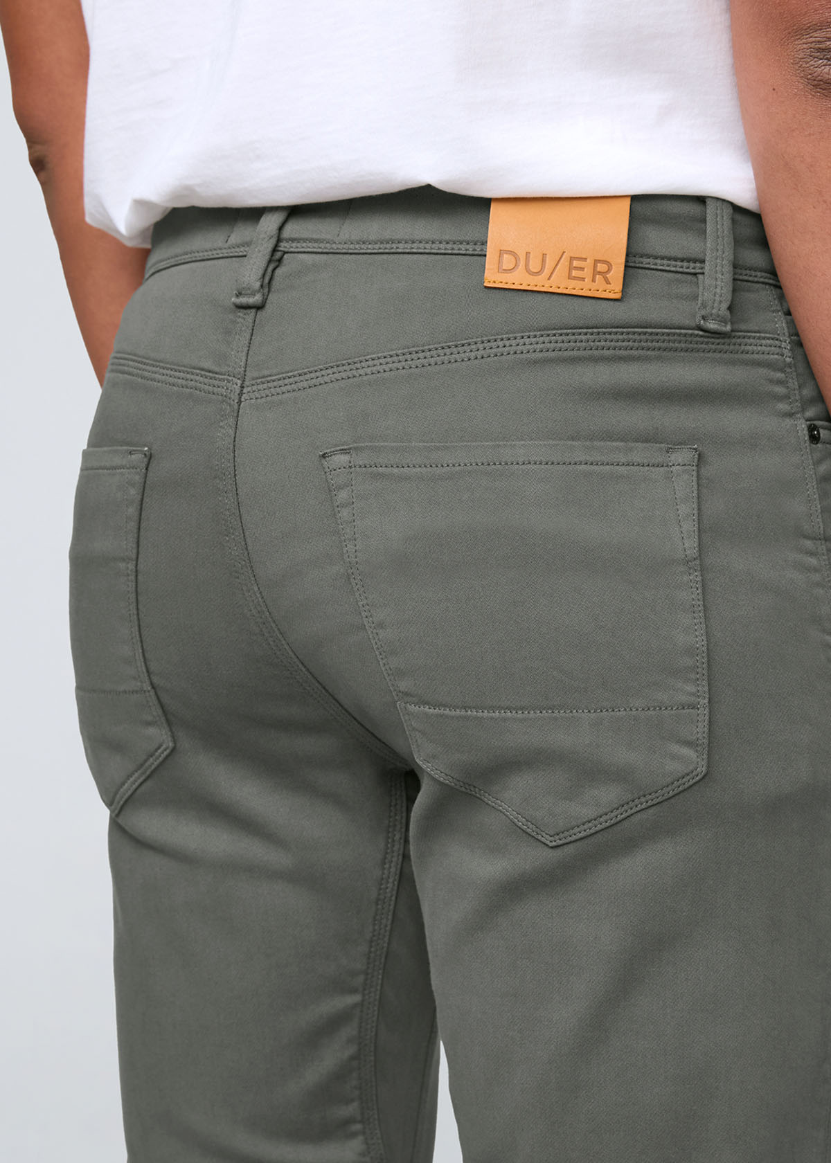 Person wearing olive green pants with a visible brand label on a white background By Duer Jeans