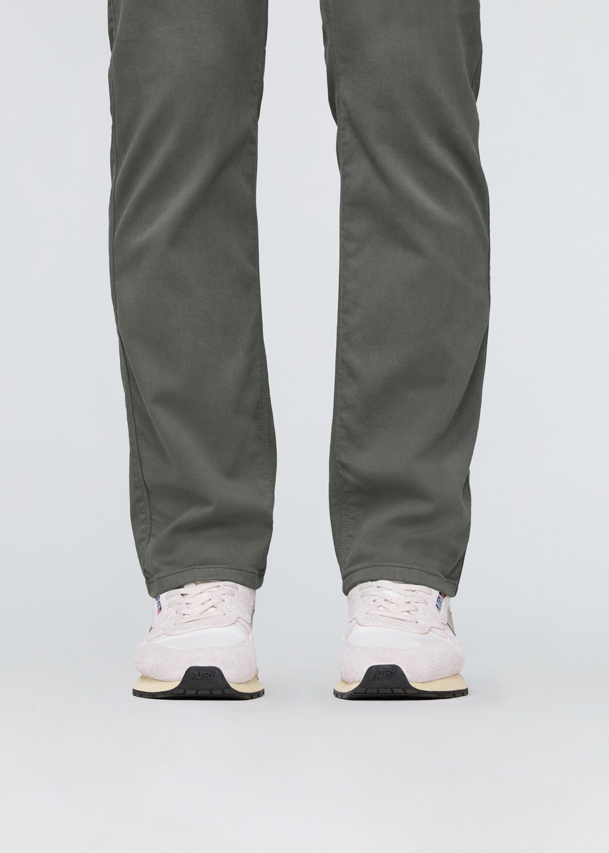 Person wearing green pants and white sneakers on a light gray background By Duer Jeans