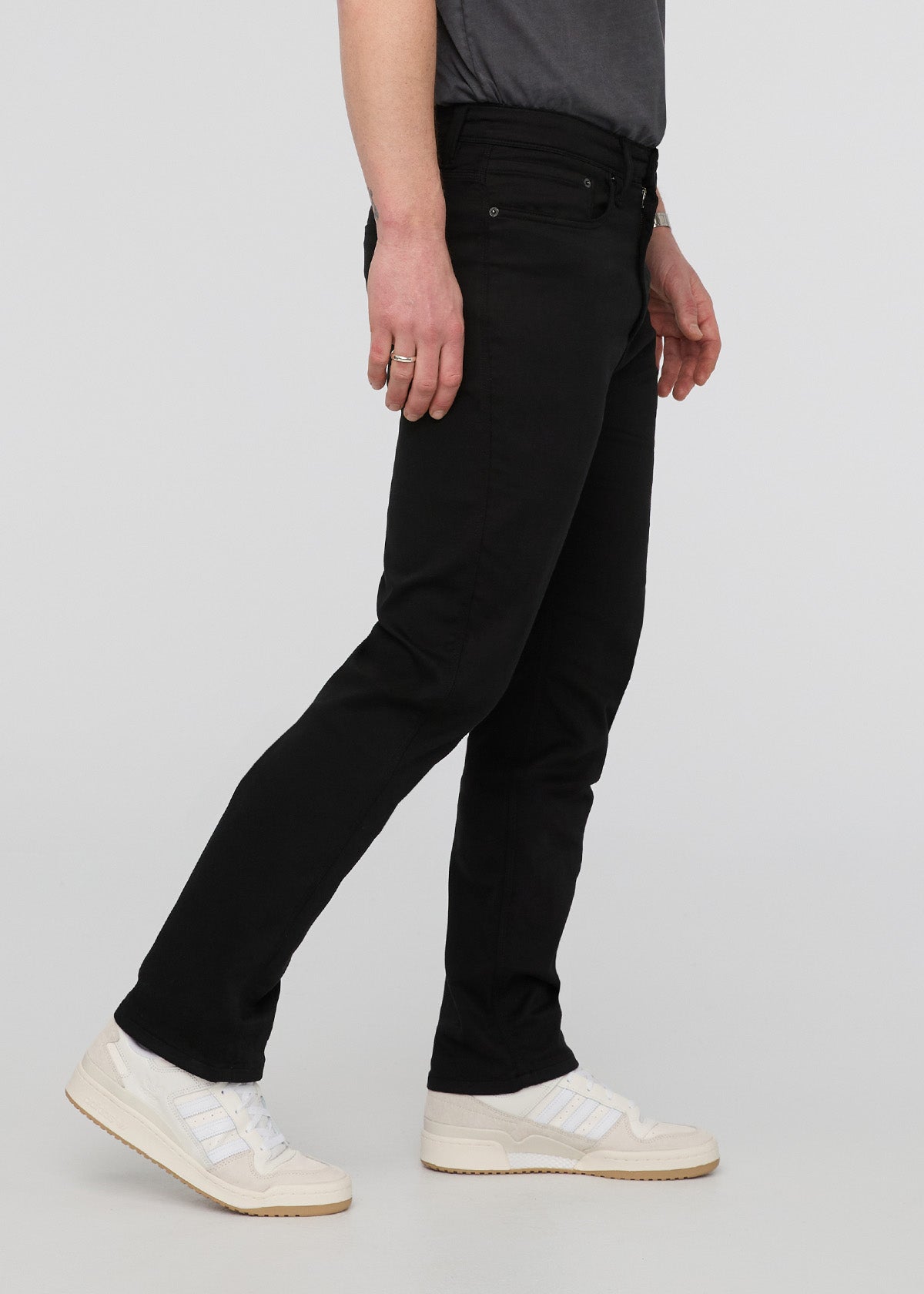 Person wearing black pants and white sneakers on a light gray background By Duer Jeans