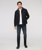 Man wearing a black jacket, white shirt, and dark jeans on a white background By Duer Jeans